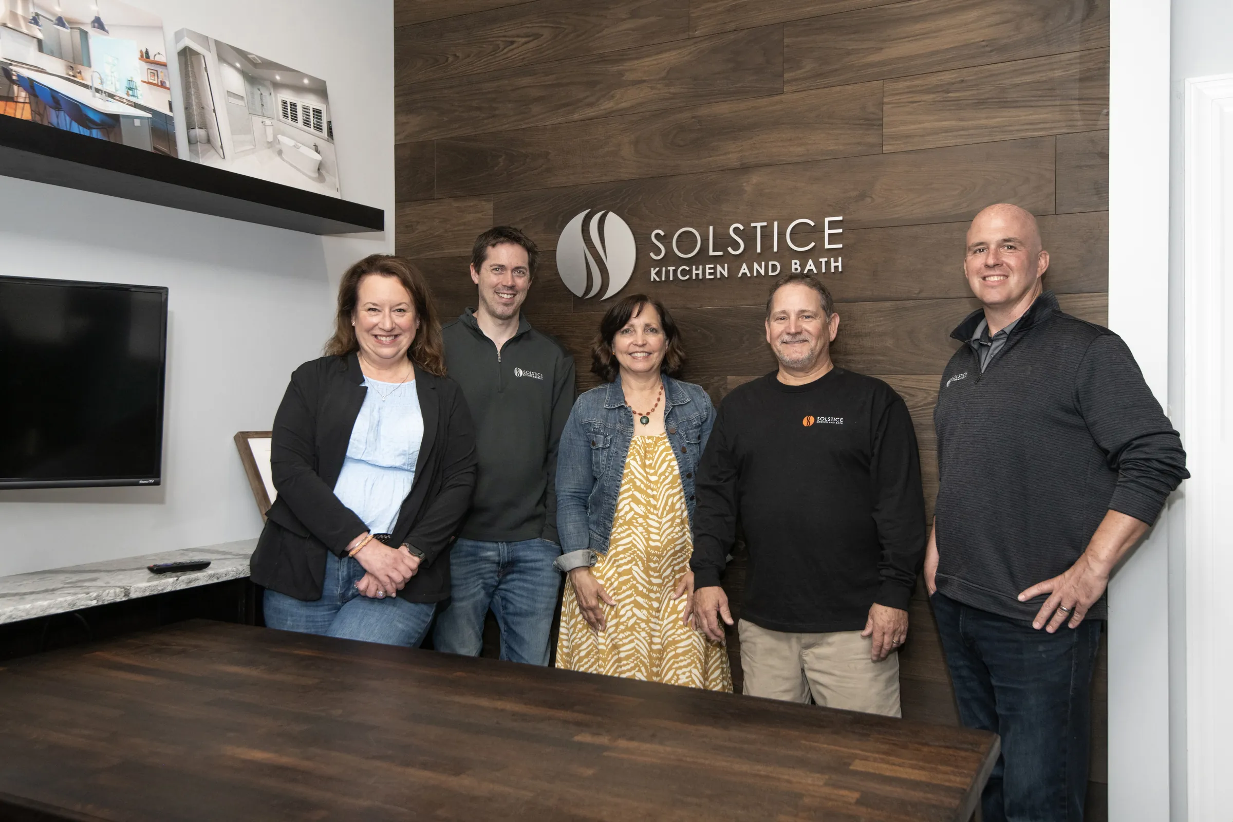 Five people standing behind a table beneath a Solstice Kitchen and Bath wall sign.