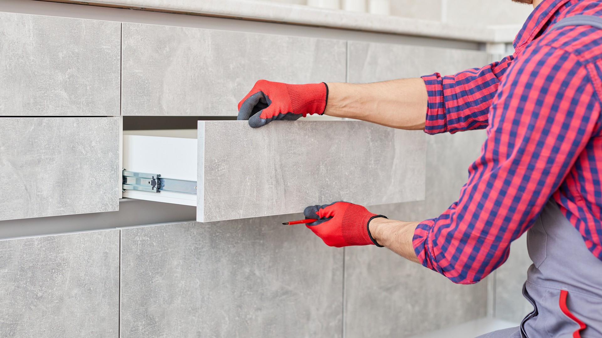 Hands adjusting a kitchen cabinet hinge during a refacing project on dated wood cabinetry in an Anne Arundel County remodel.
