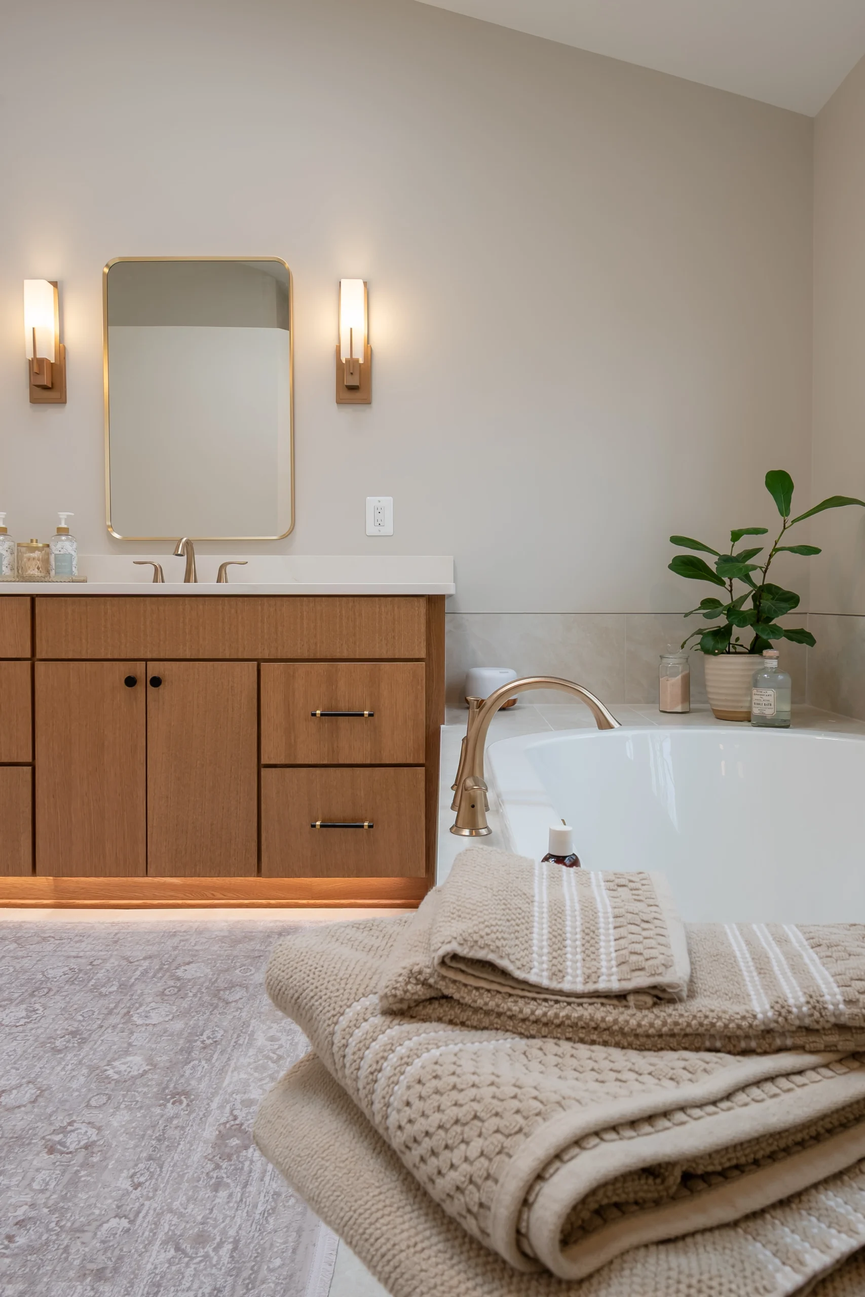 Folded towels beside a white bathtub, with a brown vanity and mirror beyond.