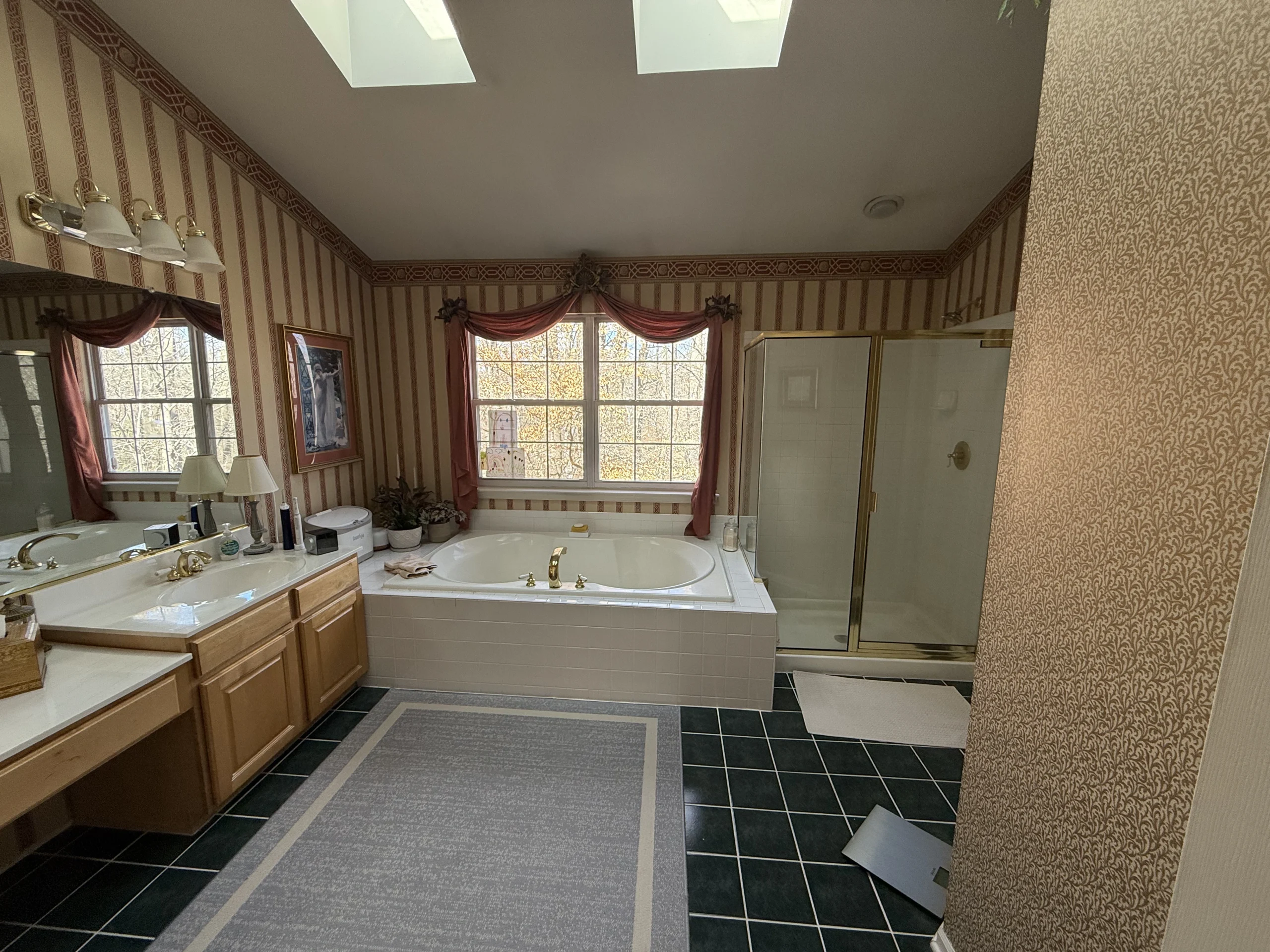 Bathroom with striped wallpaper, brown vanity cabinets, a built-in tub and an enclosed shower beneath skylights.