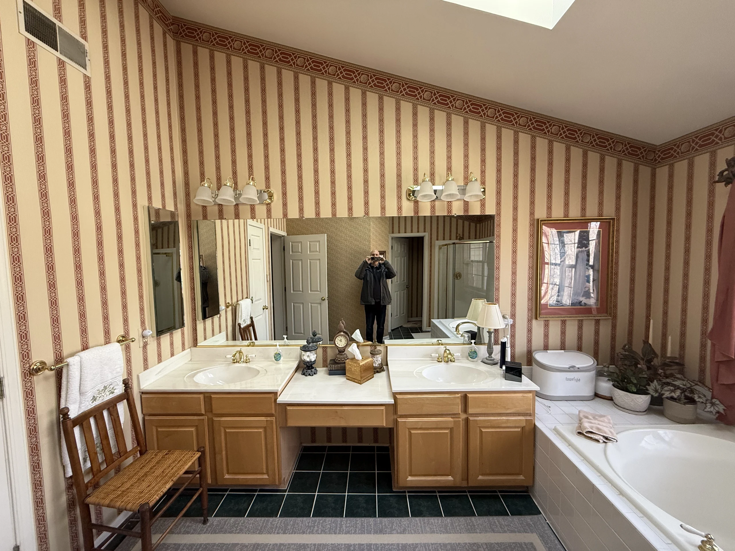 Double vanity with brown cabinets and a central seat area beneath mirrors on a striped bathroom wall.