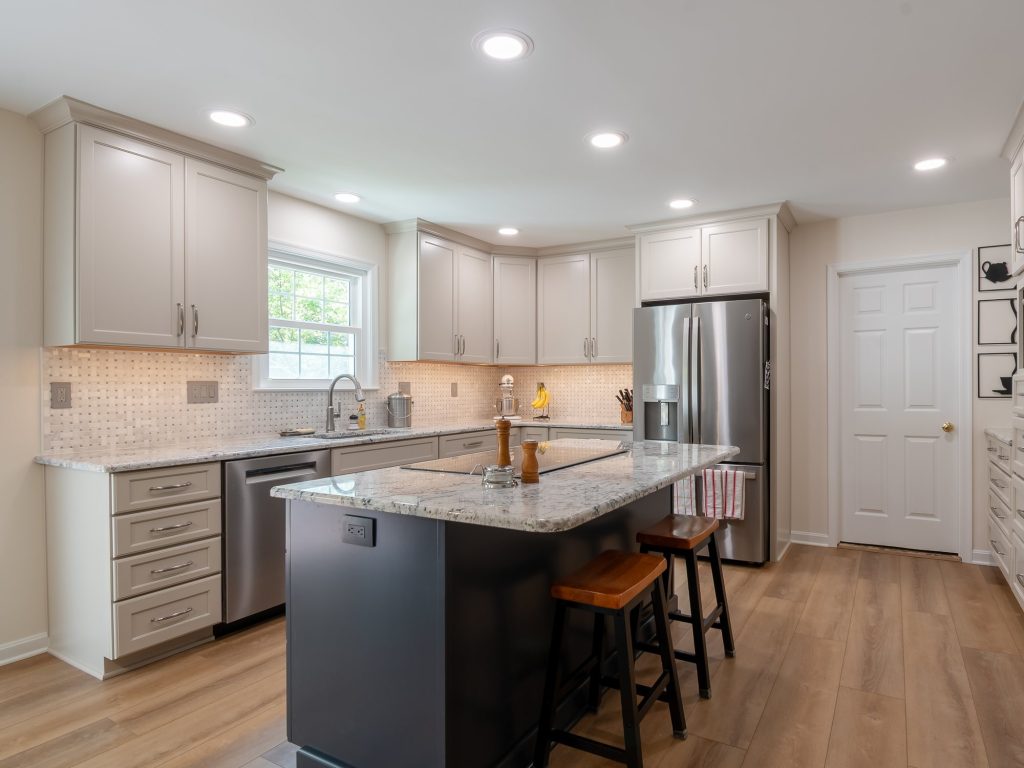 After: the same kitchen with light gray shaker cabinets, speckled white counters, a basketweave tile backsplash, a wood-look floor and a dark island that still holds the cooktop.