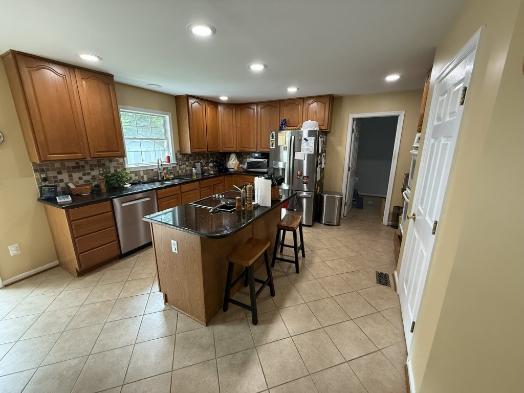 Before: kitchen with wood cabinets, black counters, a mosaic tile backsplash, a tile floor and a wood island with a cooktop and two stools.