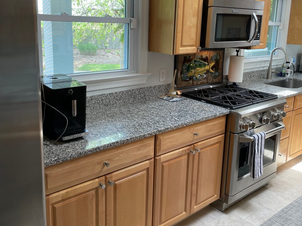 Before: galley kitchen with wood cabinets, speckled gray counters and a stainless gas range.