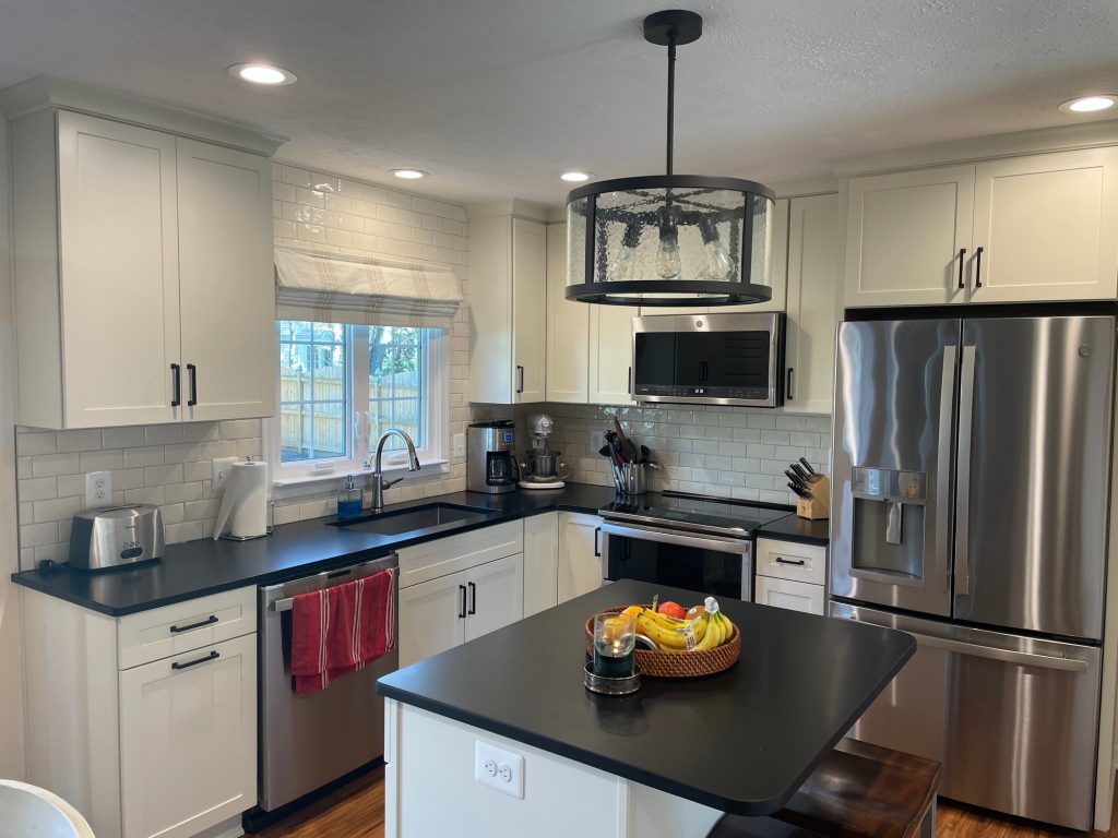 After: the same L-shaped kitchen with white shaker cabinets, dark counters, a white subway tile backsplash and stainless appliances.