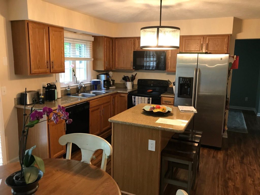 Before: L-shaped kitchen with wood cabinets, speckled counters, black appliances and a center island.